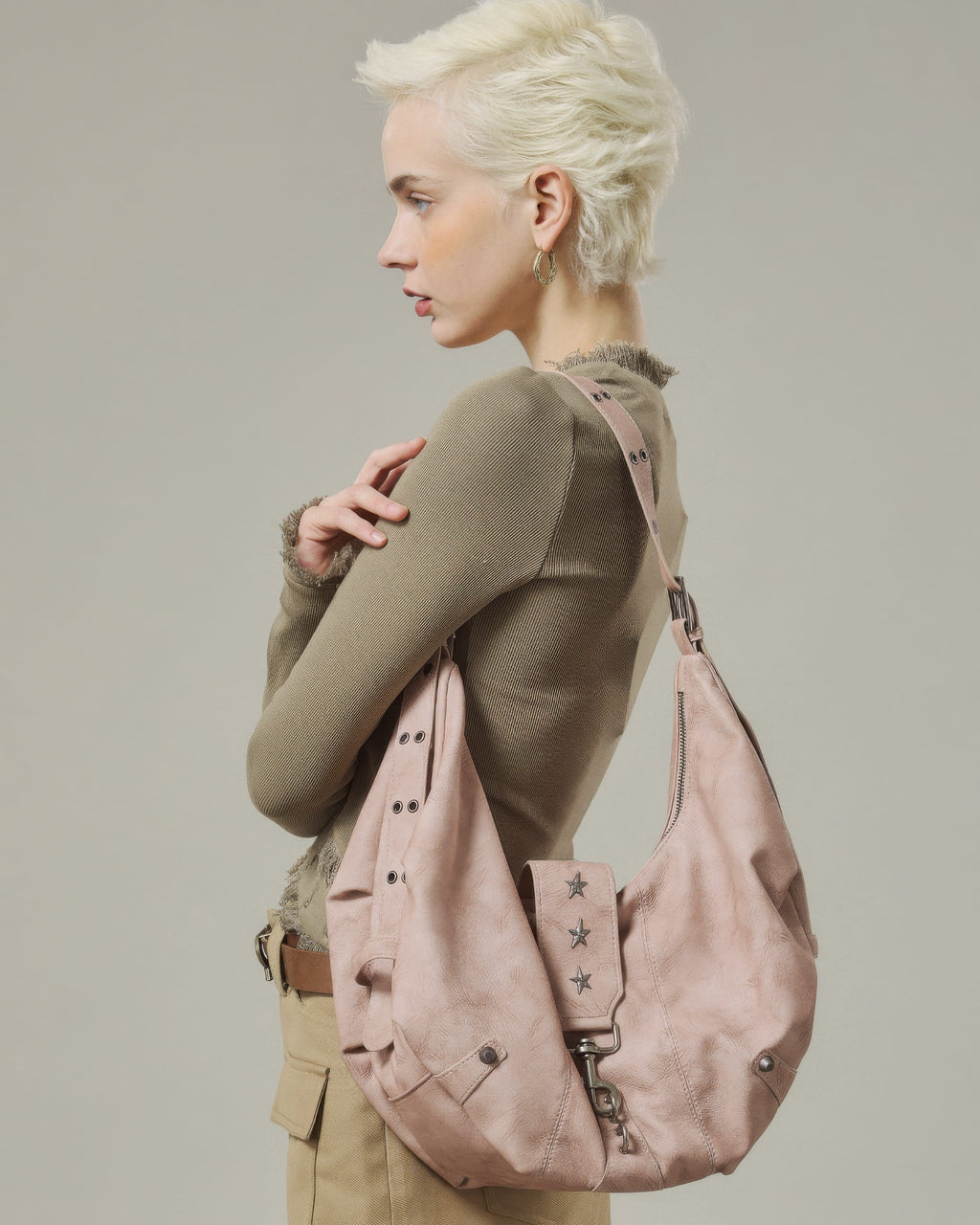 Side view shot of model wearing a blush pink crescent faux leather shoulder bag with metal grommet strap details