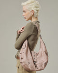 Side view shot of model wearing a blush pink crescent faux leather shoulder bag with metal grommet strap details