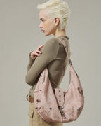 Side view shot of model wearing a blush pink crescent faux leather shoulder bag with metal grommet strap details