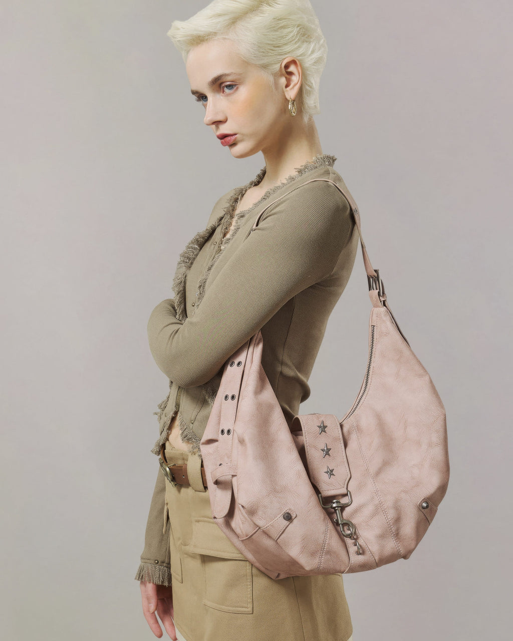 Blonde model in brown top carrying a large dusty pink slouchy hobo purse featuring star rivets and lobster clasp