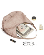 Flat lay of open dusty pink leather hobo tote filled with magazine, tablet, glasses, and beauty products