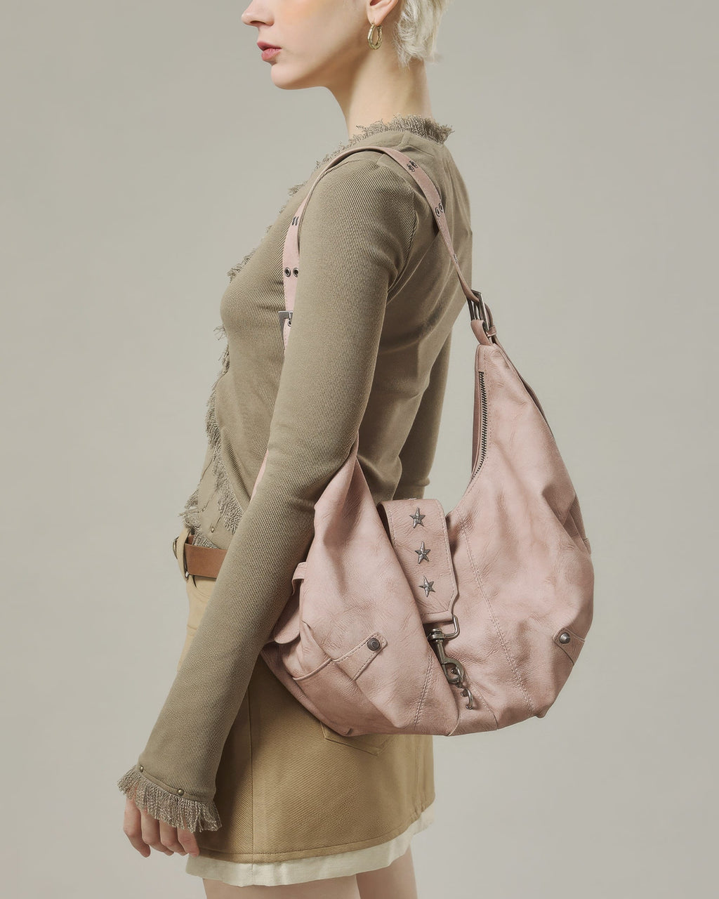 Three-quarter side view of model wearing a dusty pink slouchy crescent shoulder bag with grommet strap