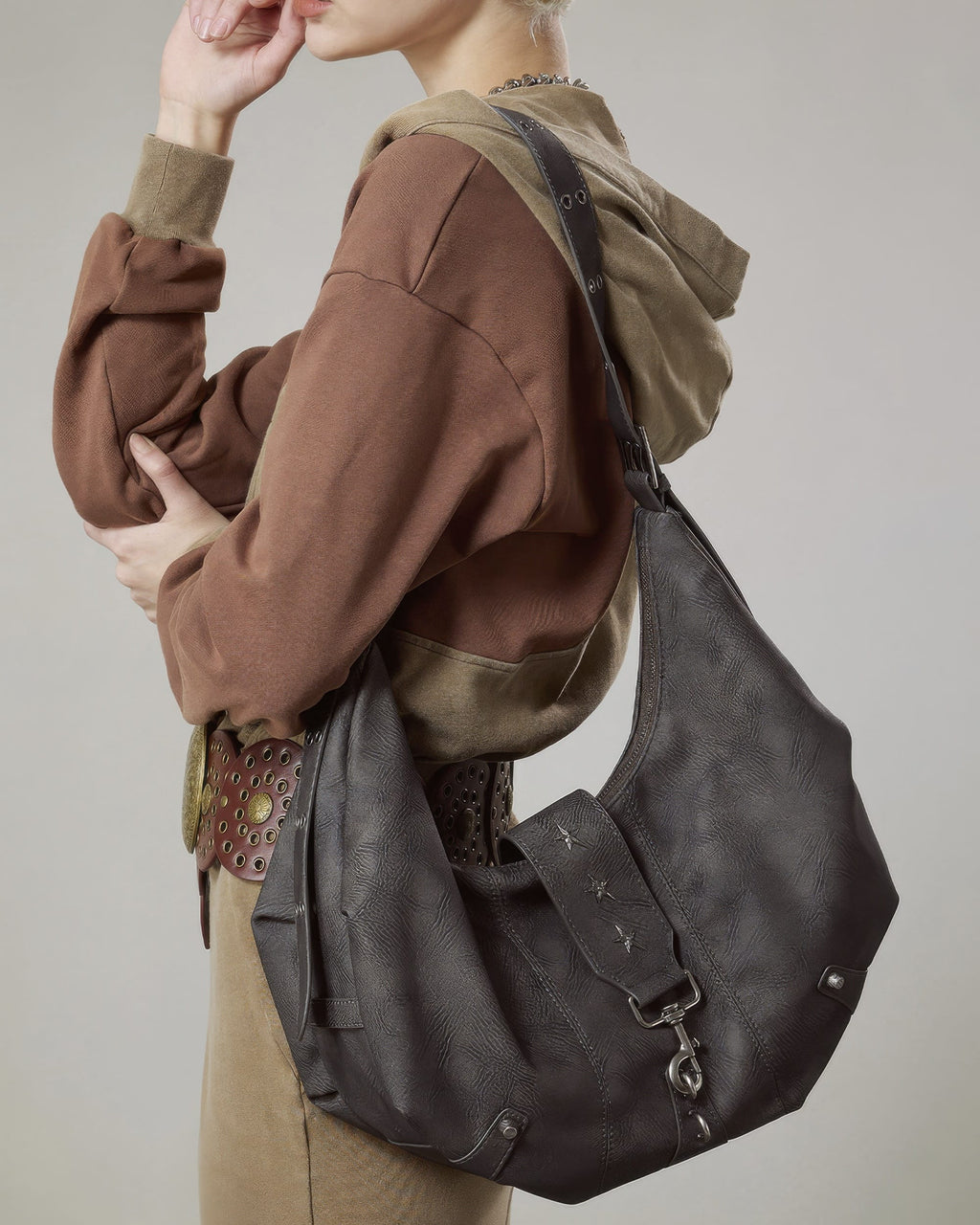 Model posing with dark grey faux leather crescent hobo bag featuring star studs and vintage buckle accents