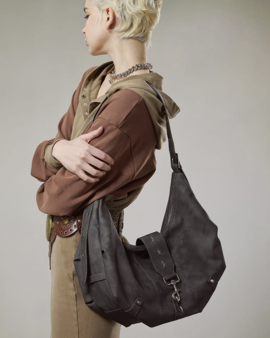 Side profile of model wearing a dark grey distressed faux leather crescent hobo bag with star rivets
