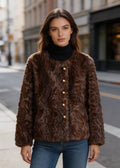 Front portrait of a woman wearing a buttoned dark brown textured faux fur coat over a black turtleneck.