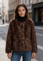 Front portrait of a woman wearing a buttoned dark brown textured faux fur coat over a black turtleneck.