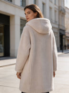Back view over-the-shoulder shot of a woman wearing a white plush hooded shearling winter coat.