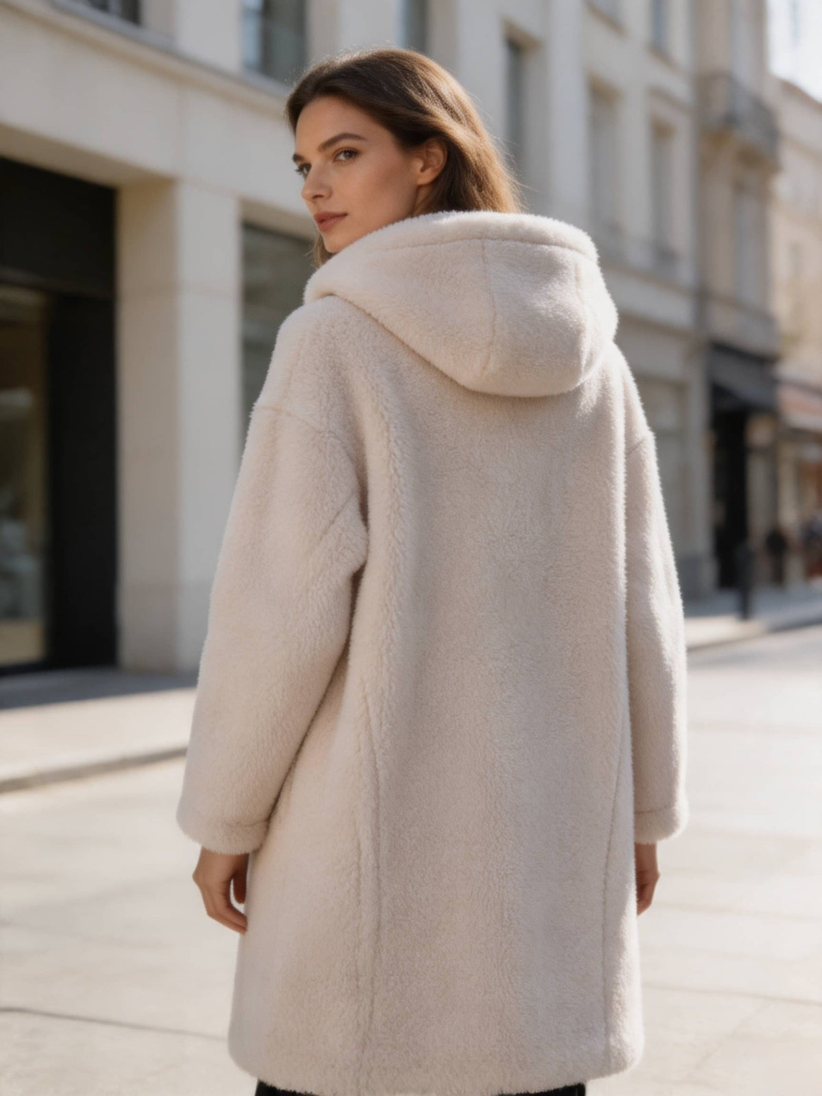 Back view over-the-shoulder shot of a woman wearing a white plush hooded shearling winter coat.