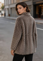 Back view of a woman wearing a taupe brown shearling wool coat with a diamond lattice pattern outdoors.
