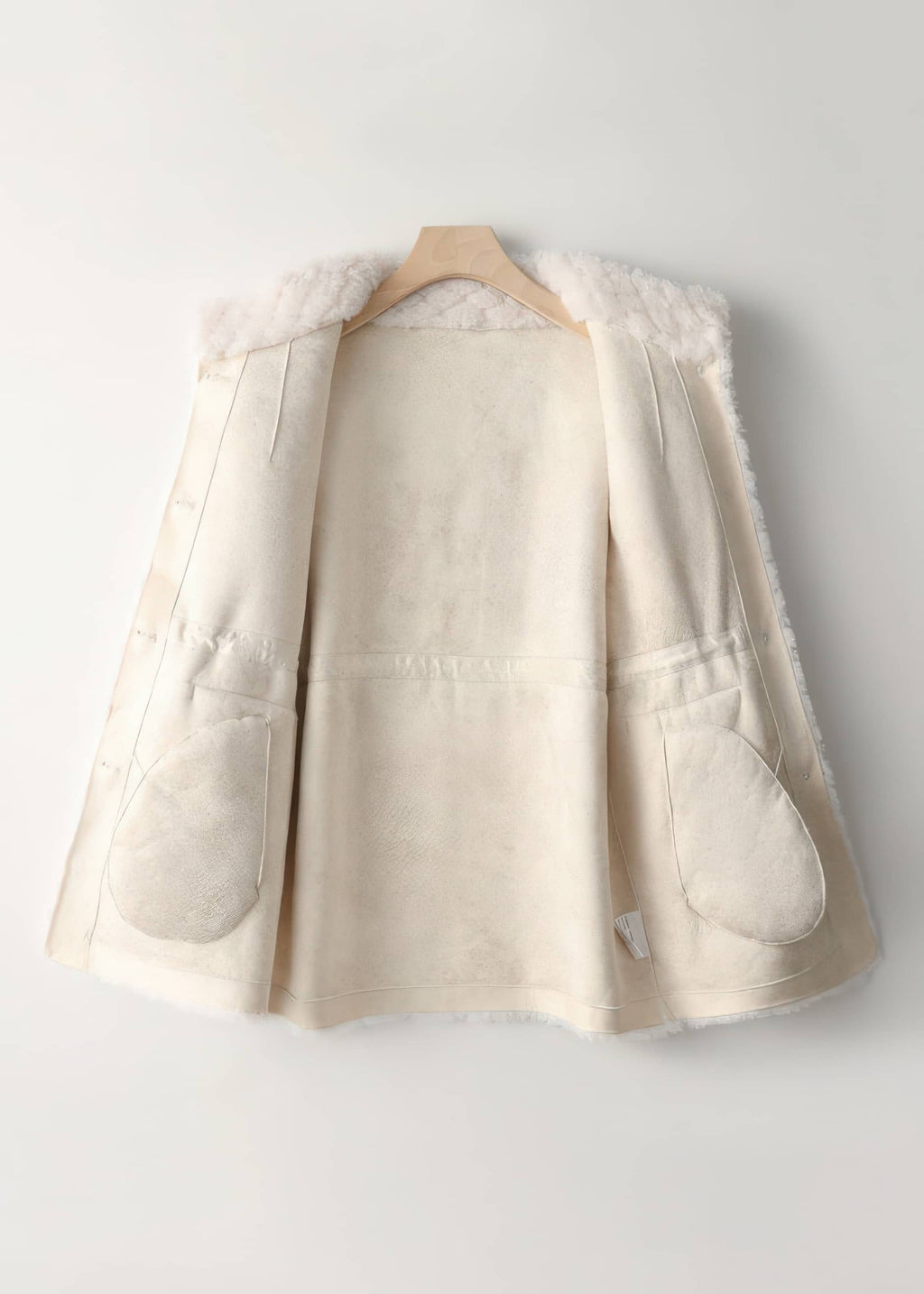 Interior suede lining detail of an off-white women's shearling coat on a wooden hanger.