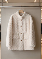 Front view of an off-white shearling wool coat featuring gold buttons and an adjustable drawstring waist on a rack.