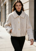 Woman walking outdoors wearing a cream fur short coat with buttons and black turtleneck