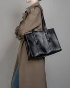 Professional lifestyle image of a black leather work tote bag for women with long adjustable straps and a structured design.