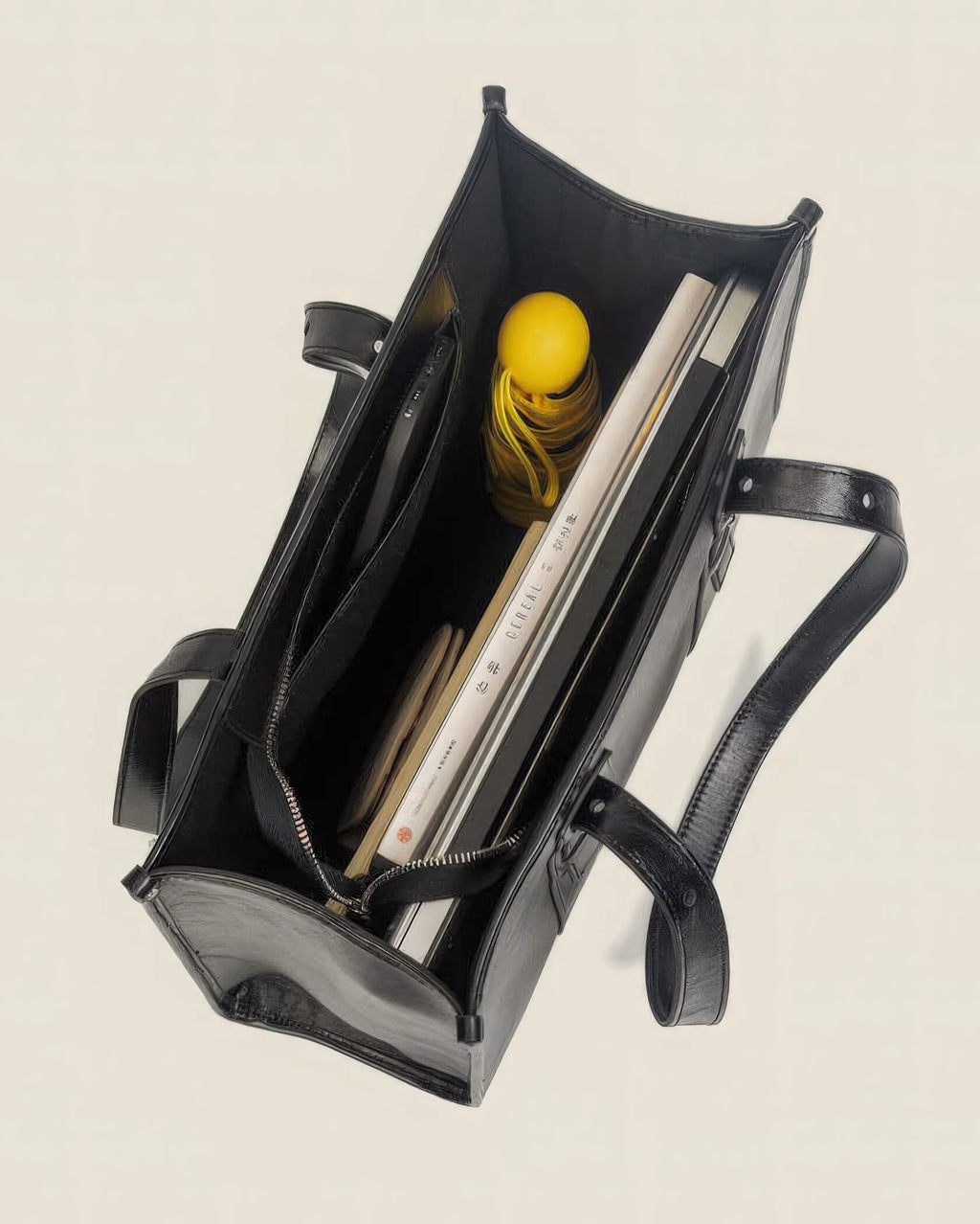 Top view of the interior of a black leather tote bag packed with a laptop, notebooks, and an umbrella to show storage capacity.
