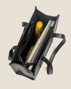 Top view of the interior of a black leather tote bag packed with a laptop, notebooks, and an umbrella to show storage capacity.