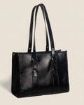 Close-up of a sleek black leather laptop tote bag for women showing the high-quality grain and adjustable strap buckles.