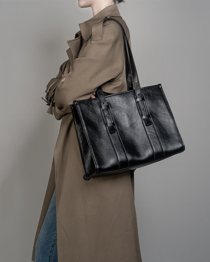 Perspective view of a structured black leather work tote bag for women featuring a glossy finish and minimalist design.