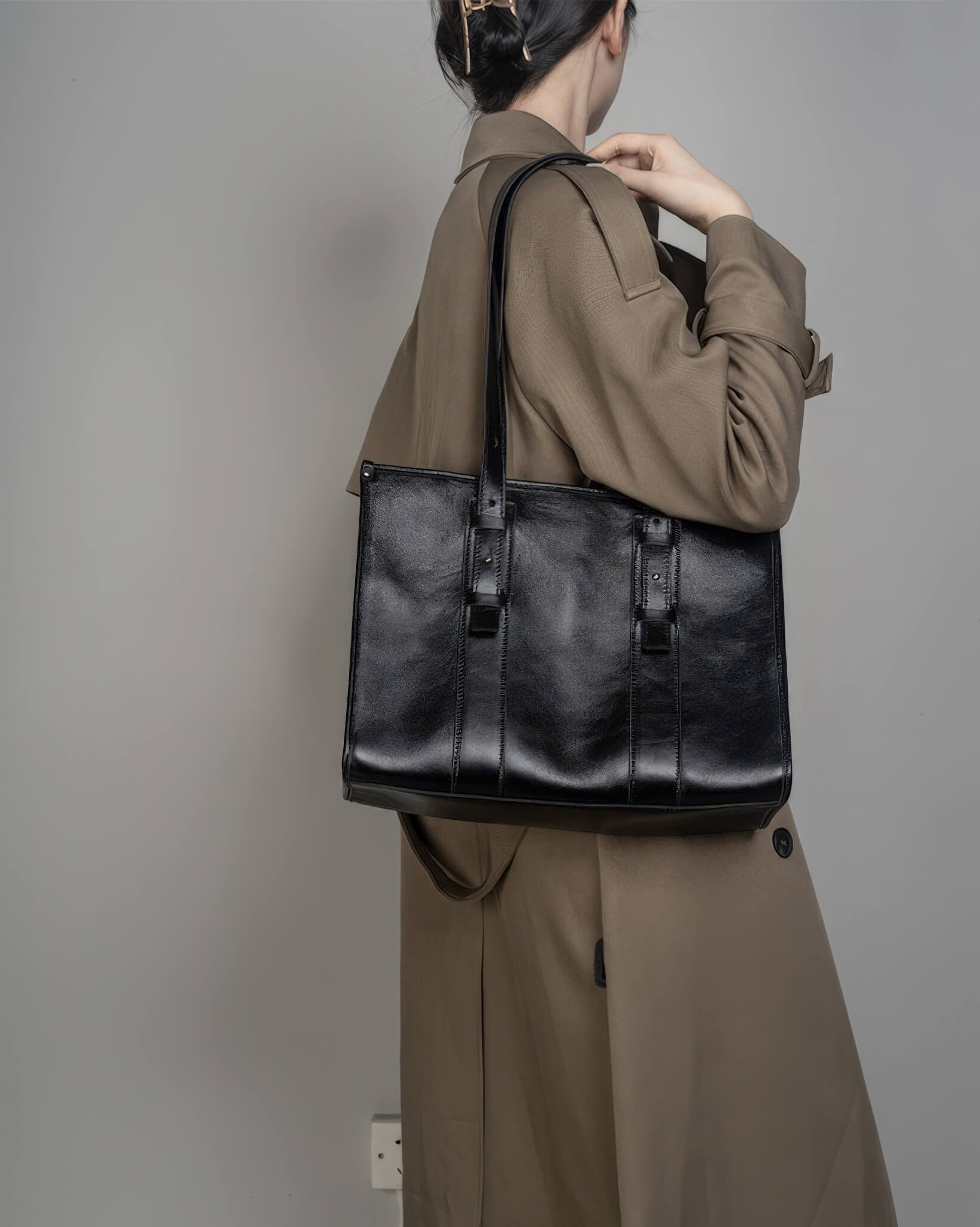Back view of a woman wearing a black leather shoulder bag, demonstrating the bag's size and fit for daily work use.