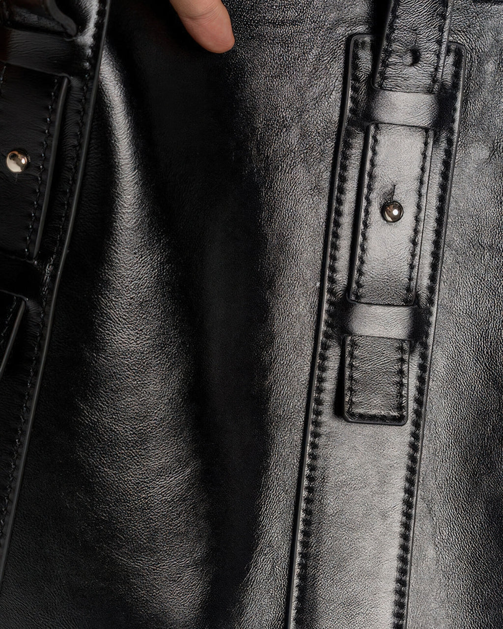 Macro detail shot of the genuine black leather texture and the silver-tone metal hardware on the tote bag's adjustable strap.
