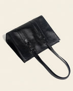 Flat lay of a black structured leather tote bag highlighting the reinforced bottom and premium stitching details.