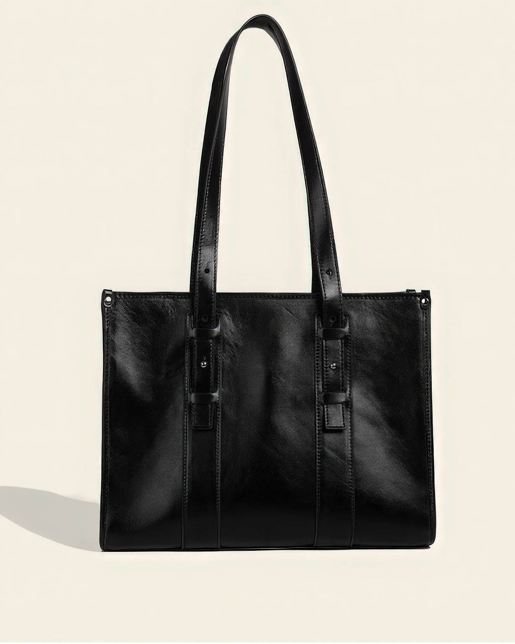 Front view of a professional black genuine leather tote bag with long adjustable shoulder straps and stud detailing.
