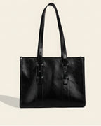 Front view of a professional black genuine leather tote bag with long adjustable shoulder straps and stud detailing.