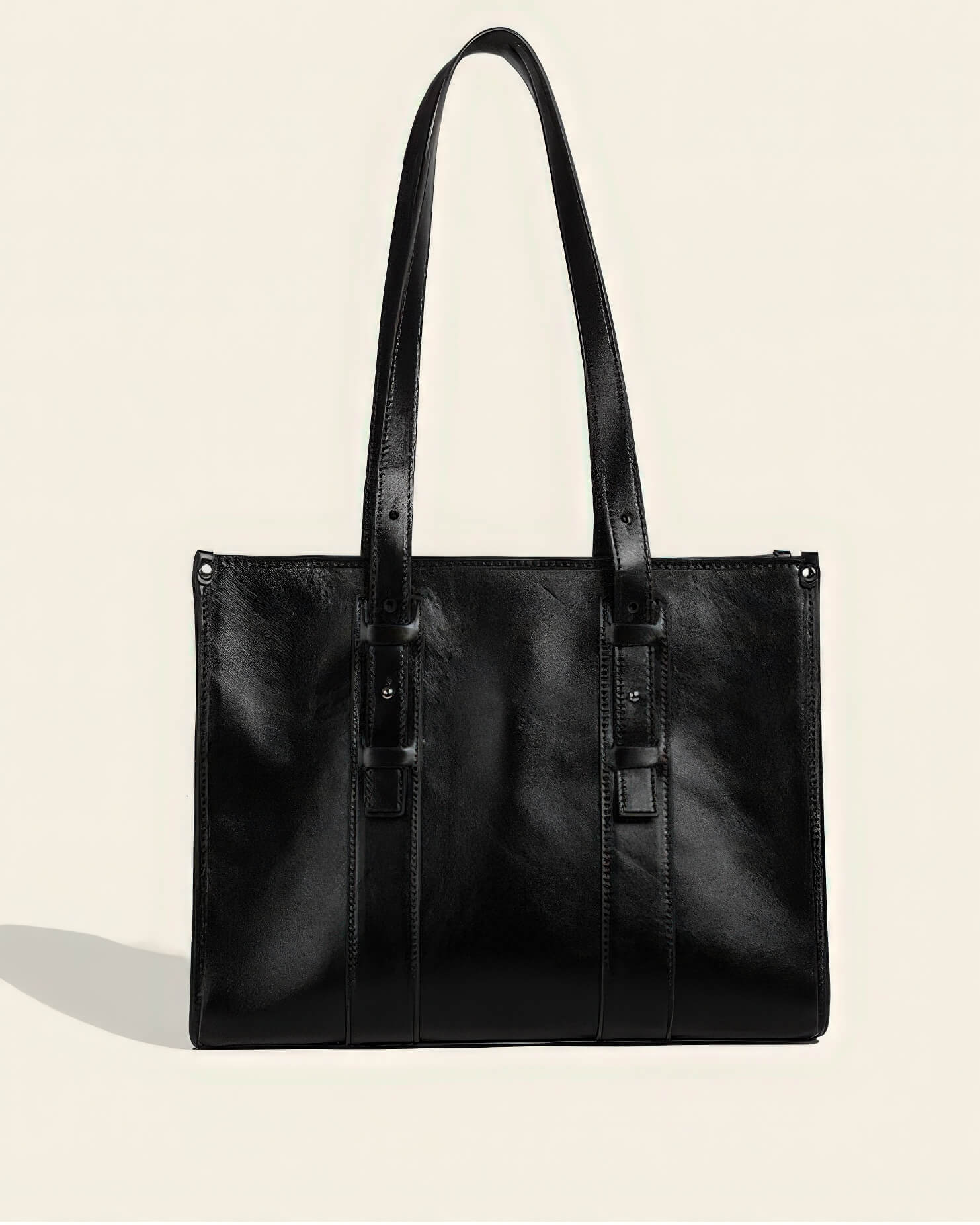 Front view of a professional black genuine leather tote bag with long adjustable shoulder straps and stud detailing.