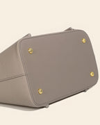 Detailed view of the structured bottom and gold-tone protective feet of a grey leather handbag.