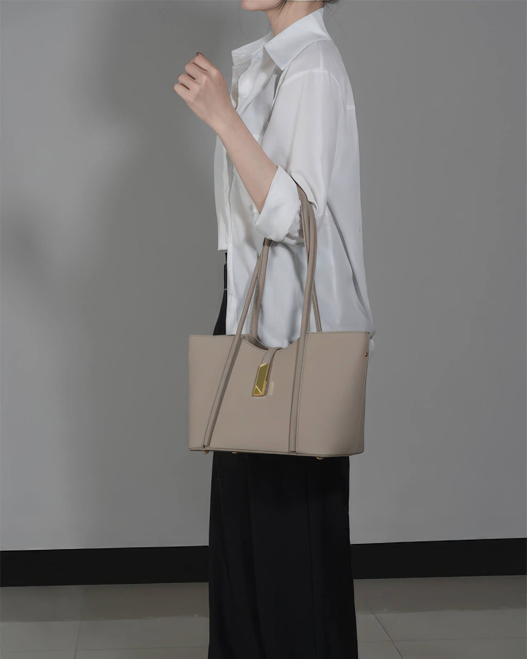 Side profile of a woman carrying a stylish grey leather laptop bag for work on her arm.