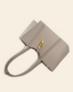 Front view of a minimalist grey genuine leather tote bag with long shoulder straps and a distinctive gold metal clasp.