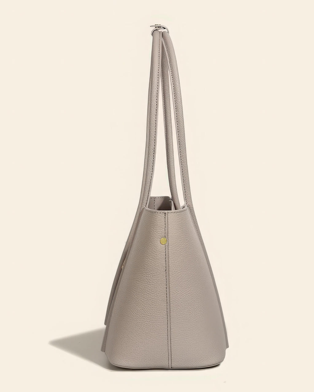 Side profile of a slim-profile grey leather tote bag showing the structural design and metal feet.