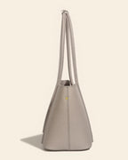 Side profile of a slim-profile grey leather tote bag showing the structural design and metal feet.