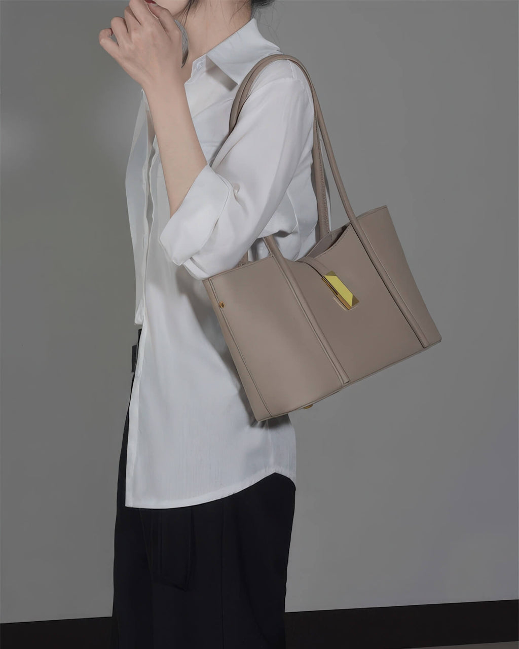 Close-up of a woman wearing a grey genuine leather shoulder bag with a gold metal accent.