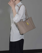 Close-up of a woman wearing a grey genuine leather shoulder bag with a gold metal accent.