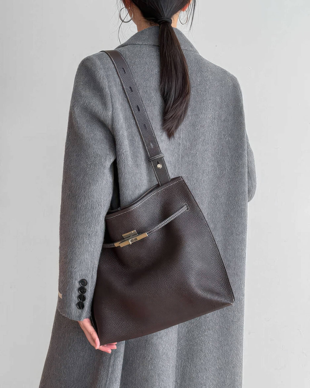 Side view of a woman wearing a grey cable knit cardigan with a mahogany leather handbag.