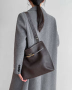 Side view of a woman wearing a grey cable knit cardigan with a mahogany leather handbag.