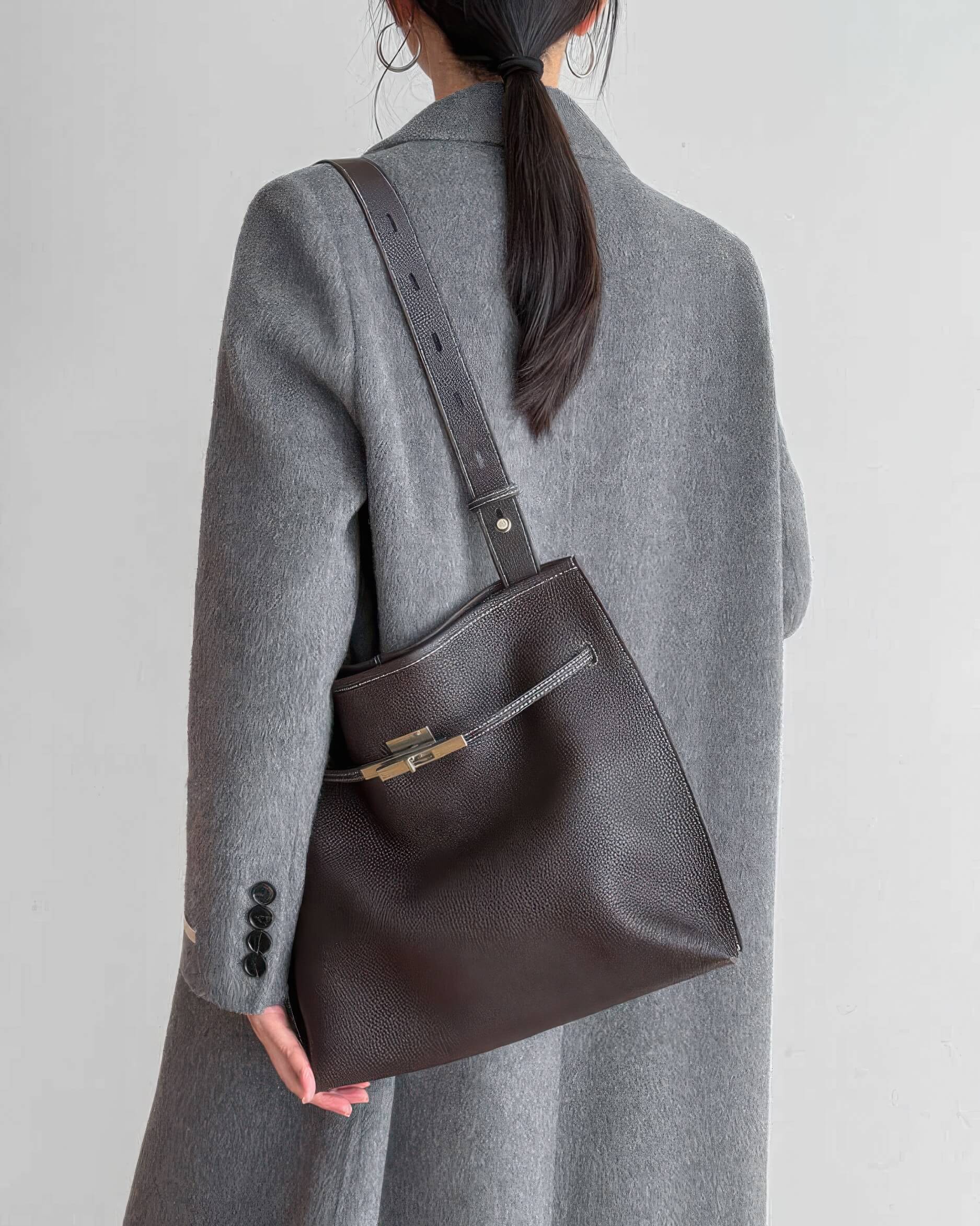 Side view of a woman wearing a grey cable knit cardigan with a mahogany leather handbag.