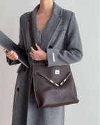 Side profile of a slim burgundy leather satchel with long shoulder straps.