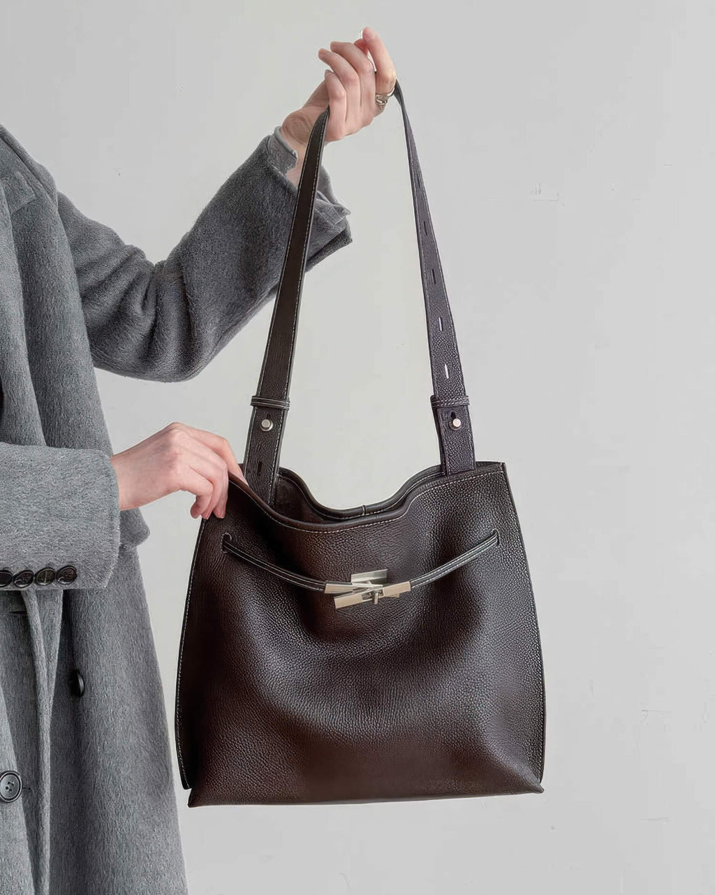 Aesthetic lifestyle shot of a woman tucking a burgundy leather underarm bag.