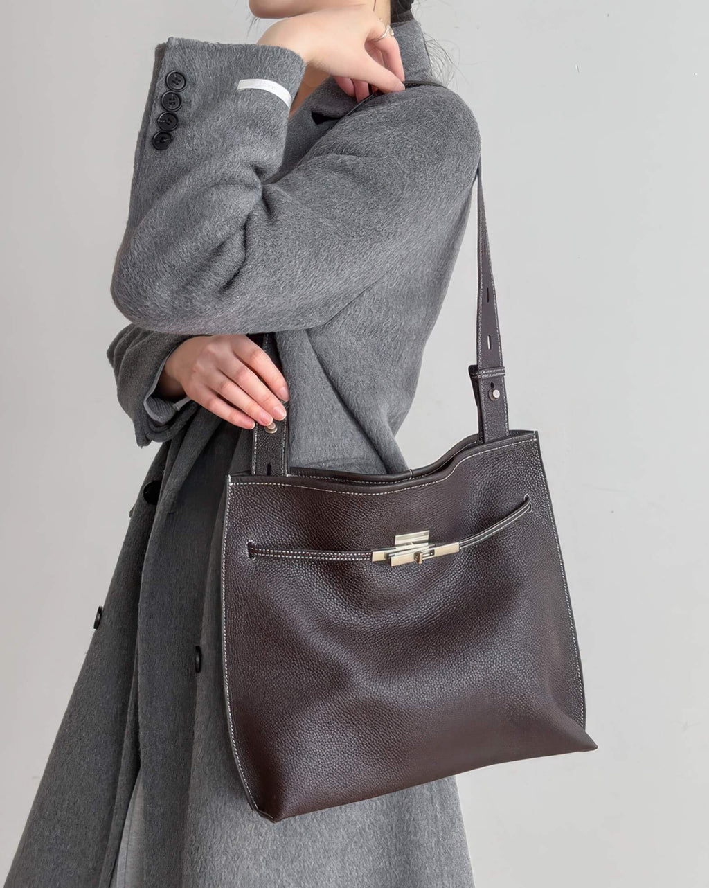 a model carrying a large mahogany leather shoulder bag over a grey sweater.
