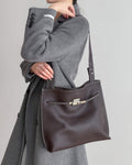 a model carrying a large mahogany leather shoulder bag over a grey sweater.