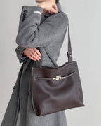 a model carrying a large mahogany leather shoulder bag over a grey sweater.