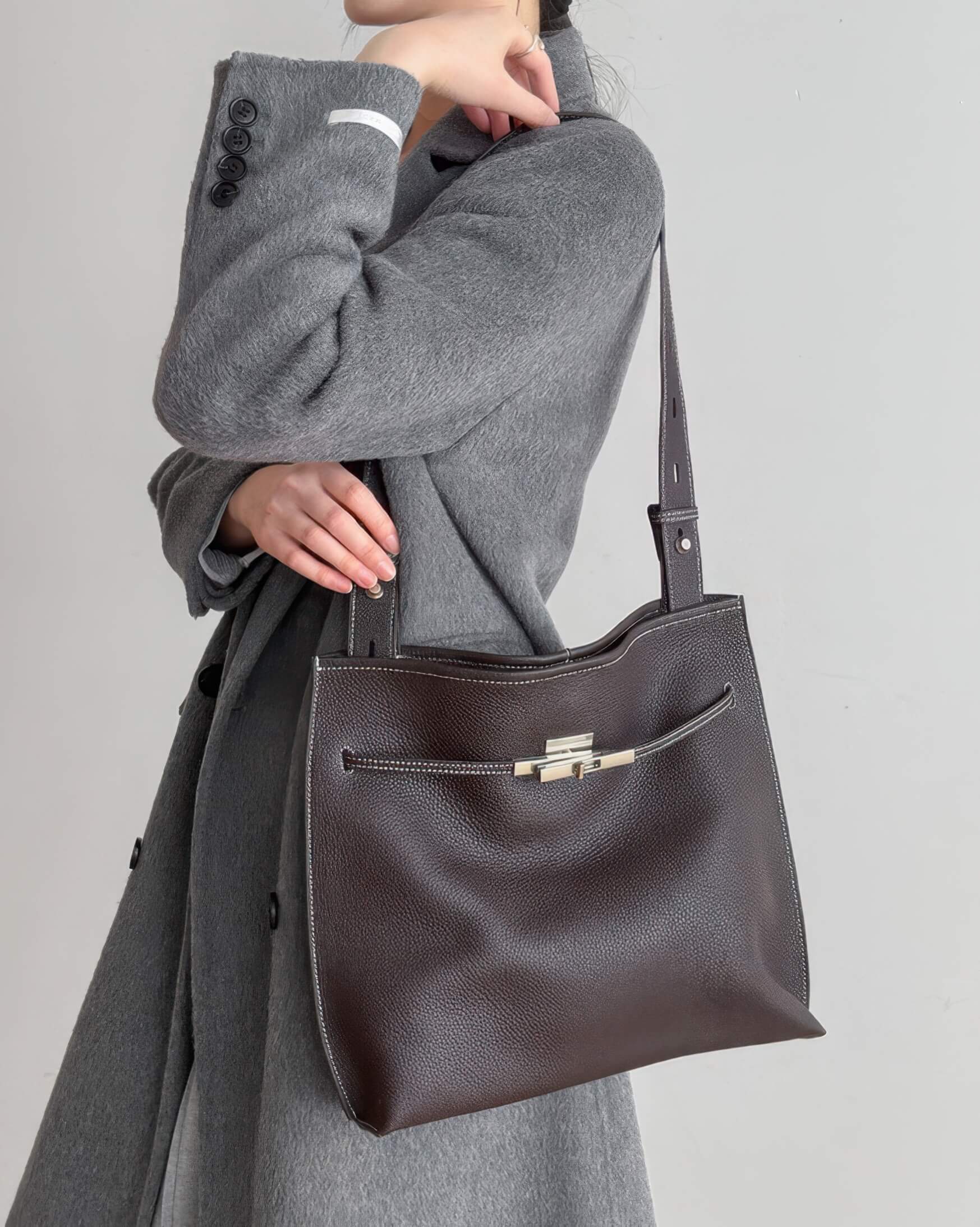 a model carrying a large mahogany leather shoulder bag over a grey sweater.
