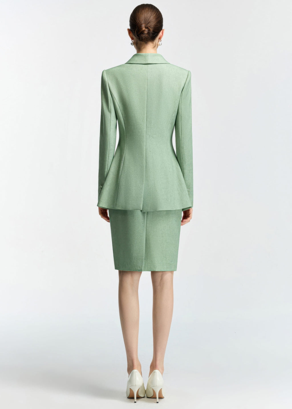 A rear view of the model wearing the mint green blazer and skirt set, showing the structured tailoring and peplum-style flare at the back of the blazer.