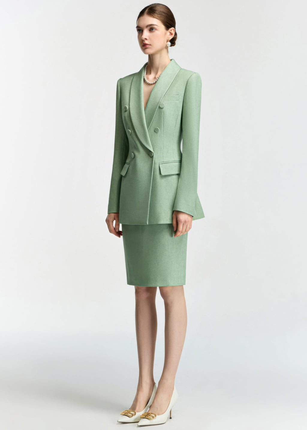A full-body shot of the model standing at a three-quarter angle, showcasing the length of the blazer and the fit of the matching skirt.