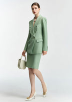 An action-style pose of the model walking or leaning slightly, holding the cream handbag, which provides a dynamic view of the mint green suit.