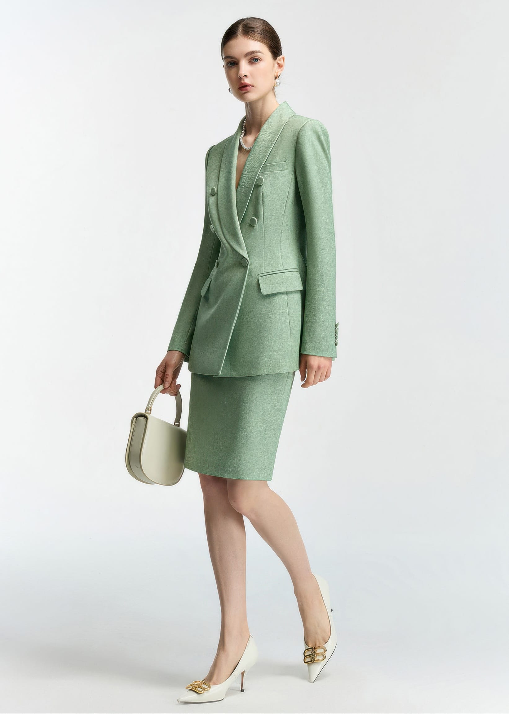 An action-style pose of the model walking or leaning slightly, holding the cream handbag, which provides a dynamic view of the mint green suit.