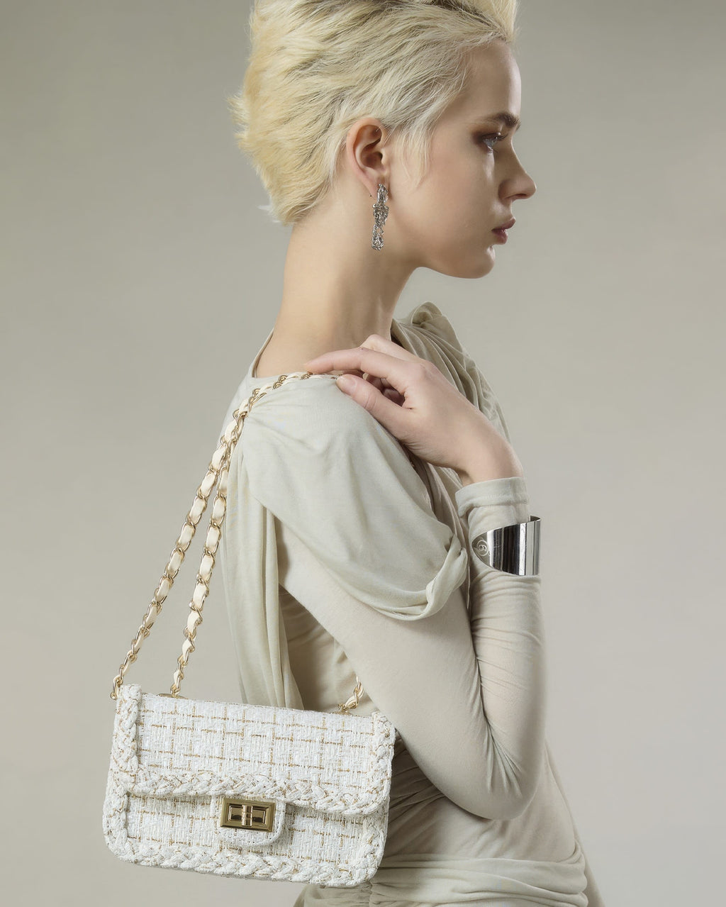 Model with blonde short hair carrying cream woven tweed shoulder bag with woven chain strap side view