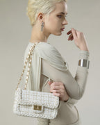 Model posing with cream woven tweed flap handbag featuring gold hardware and braided border