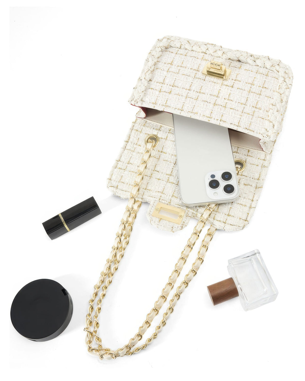 Top view flat lay of open cream tweed purse filled with smartphone lipstick and perfume bottle
